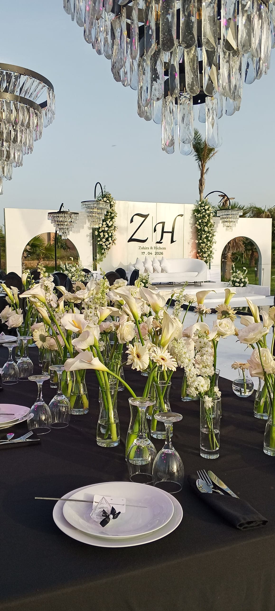 Table de réception dressée face à la scène d'un mariage, arums et roses blancs, lustres en cristal — scénographie MOYA DÉCO au Maroc